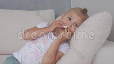 一个小女孩在软榻上吃着爆米花，看着电<strong>视屏</strong>幕。